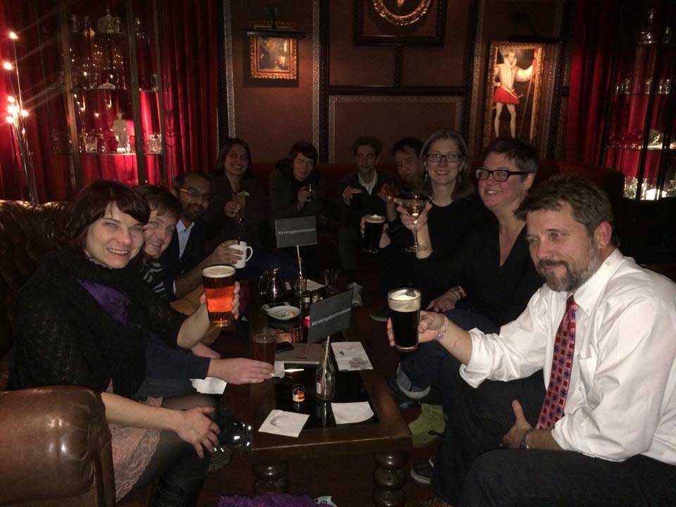 A photo of a group of museum professionals holding up drinks in a dimly lit bar. I'm in the background holding up a mug of chamomile tea.