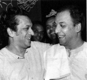 An old black and white photo of Panditji Ravi Shankar and Ustad Vilayat Khan arm-in-arm smiling at each other