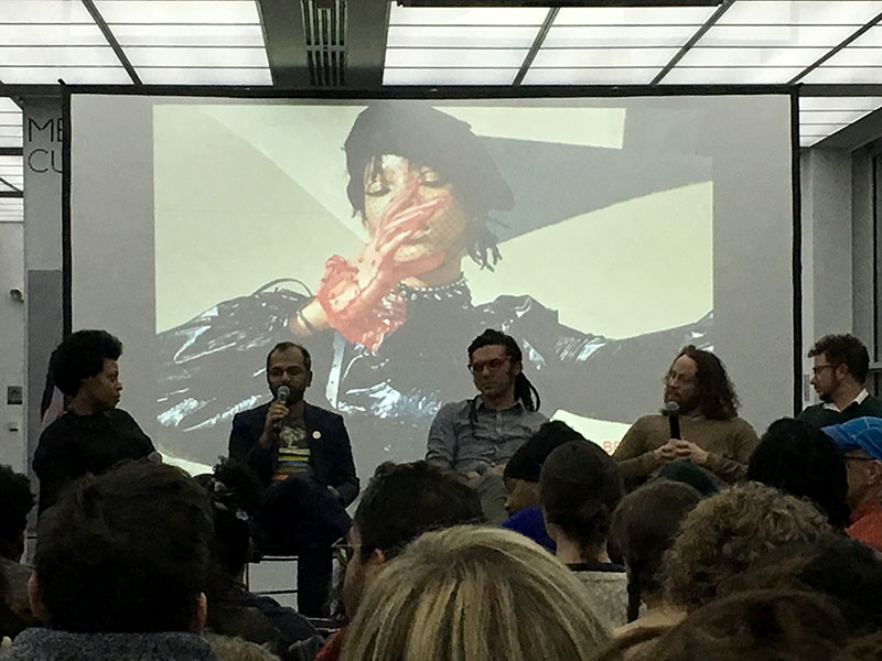 Kamilah, nikhil, Brett, Anthony and Oli seated on a stage while nikhil speaks into a microphone. A large photo of Willow Smith standing in a dramatic pose is projected behind them.